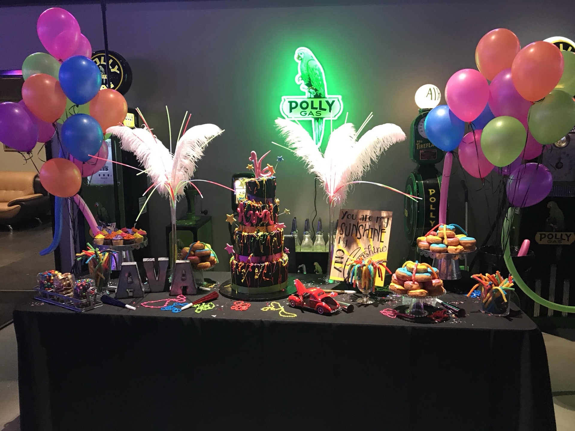 Colorful birthday party with neon Polly Gas sign, balloons, and decorated cake at Highway 39 Event Center