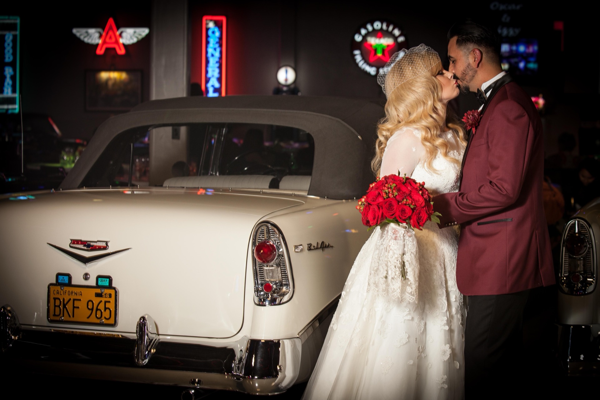 Wedding couple sharing a kiss beside a classic '55 Bel Air with neon signs at Highway 39 Event Center