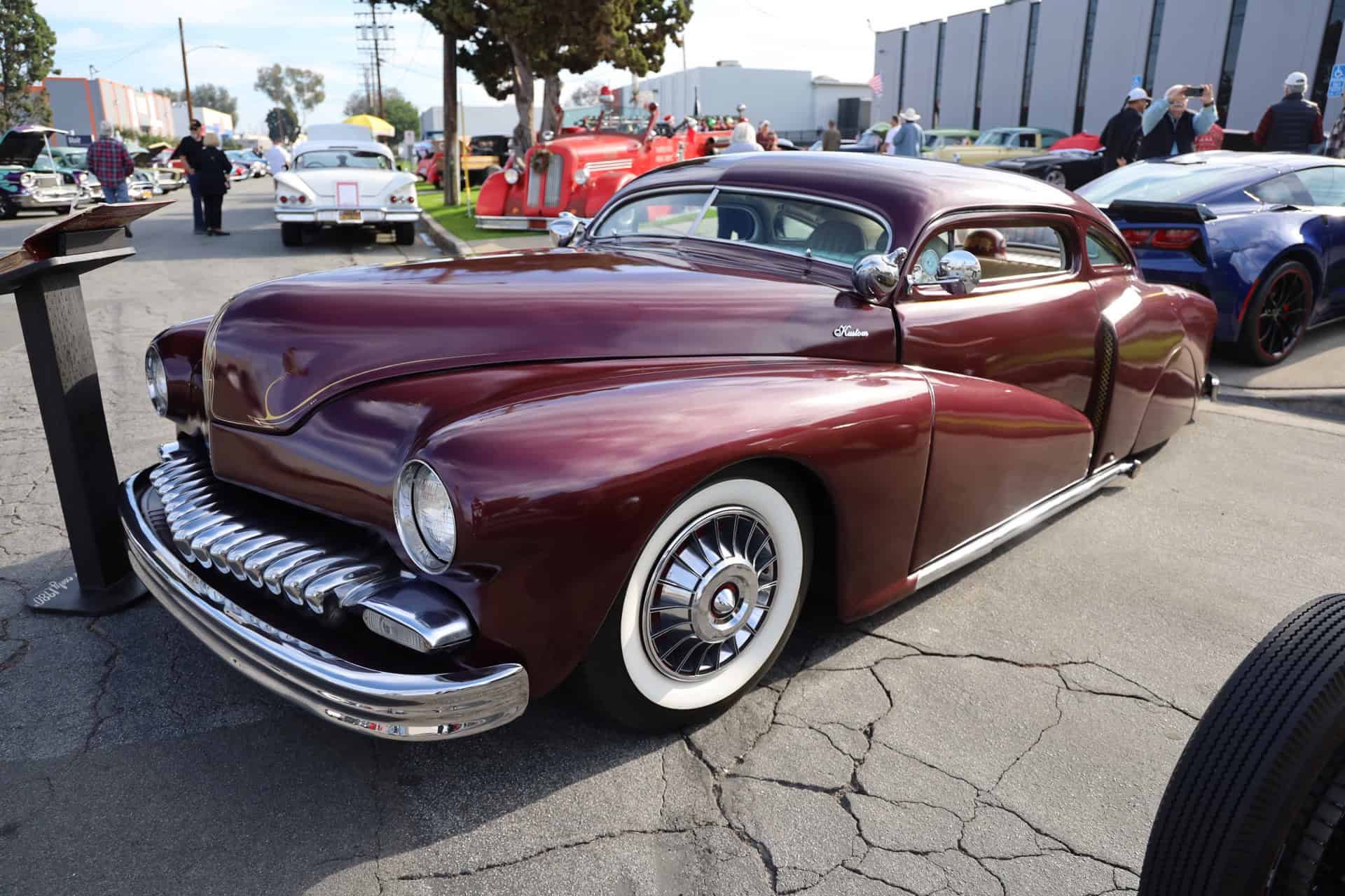 Classic 1950s car with sleek maroon finish, chrome details, and whitewall tires at the car show.